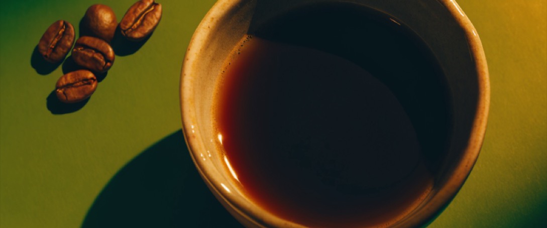 A cup of black coffee photographed from above beside roasted beans