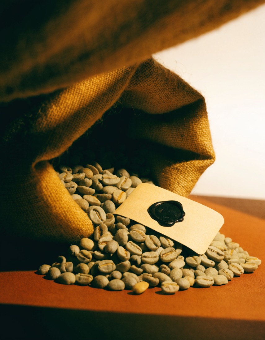 Green coffee beans spilling from a jute sack beside a blank sealed lot tag